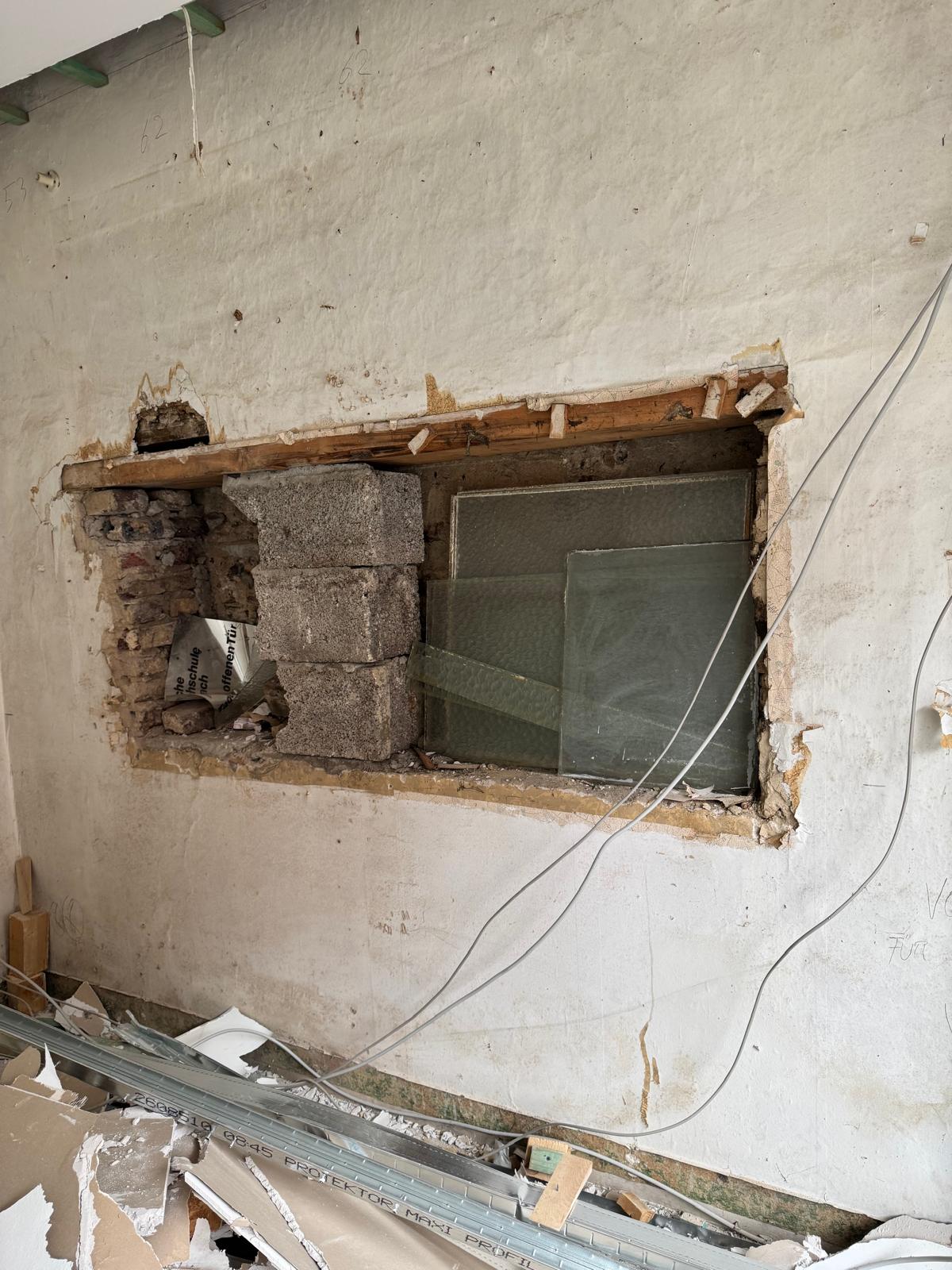 Wanddurchbruch im Rohbau mit alten Glasscheiben und Bauschutt.